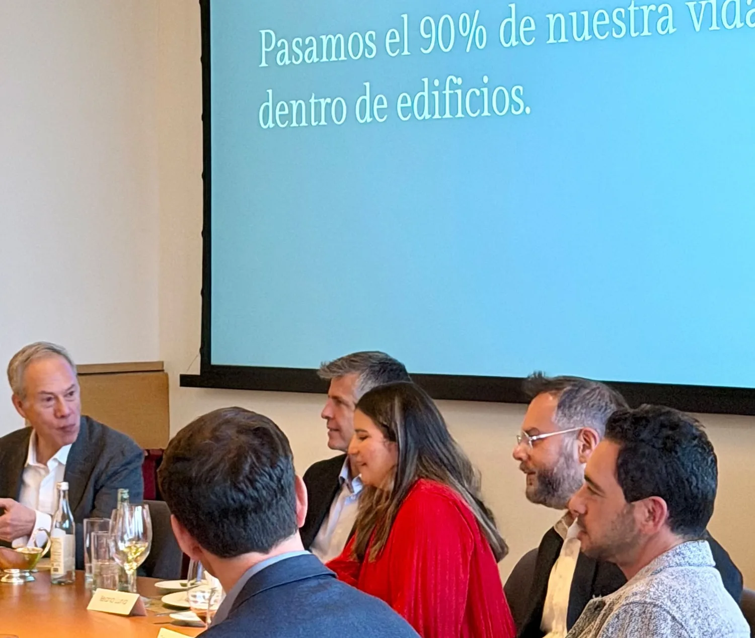 Asistentes alrededor de la mesa redonda escuchando a un ponente, con la presentación “Pasamos el 90% de nuestra vida dentro de edificios” en la pantalla detrás de él, sesión inaugural de WRE Circle en la Ciudad de México