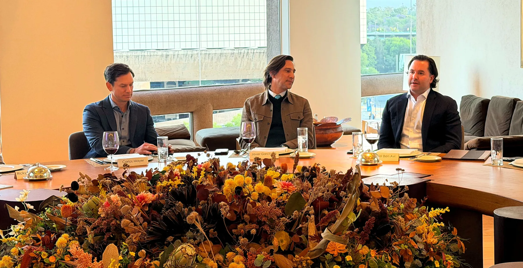 Three members in conversation at the round table in front of the window, a large dried floral arrangement in the foreground, at the inaugural WRE Circle gathering in Mexico City